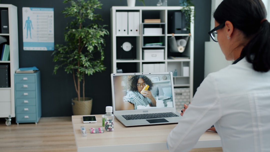 Young woman in doctors uniform is talking to sick African American girl online using laptop in clinic giving medical advice. People and healthcare concept.